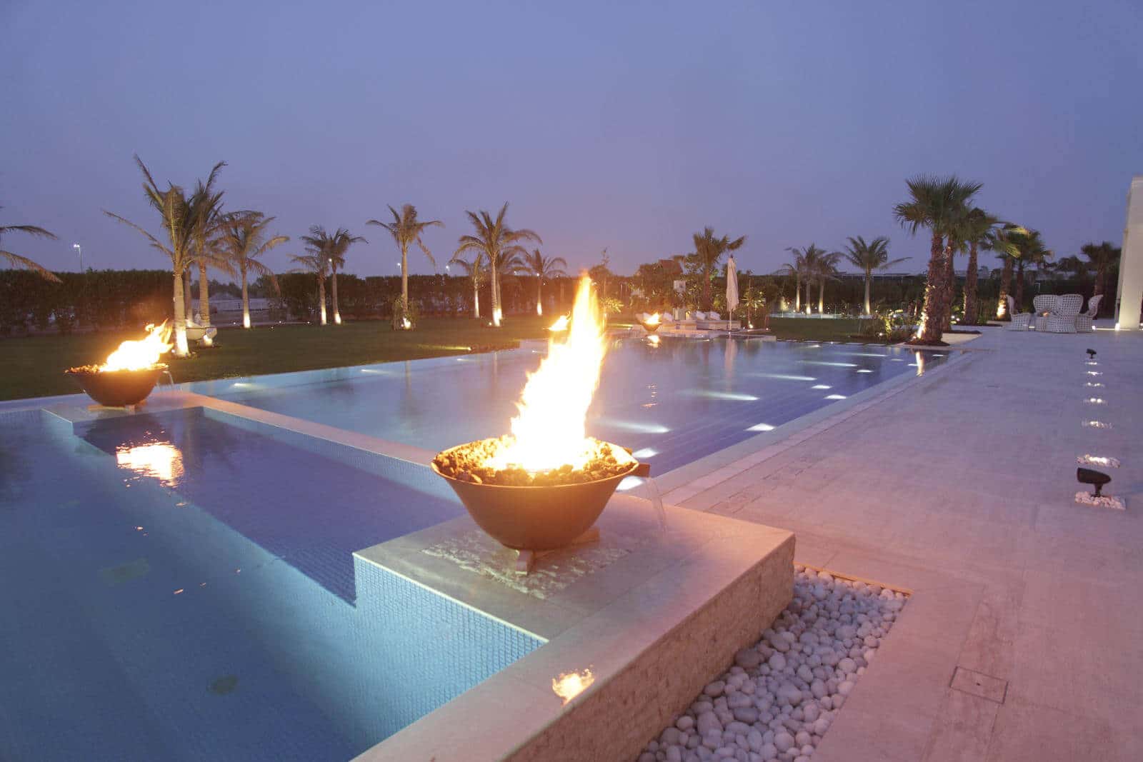 Pool and garden lighting with fire bowls at dusk, controlled by Crestron, private estate, Dubai